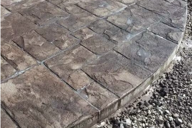 edge of a Stamped concrete pavement pad meeting decorative rocks